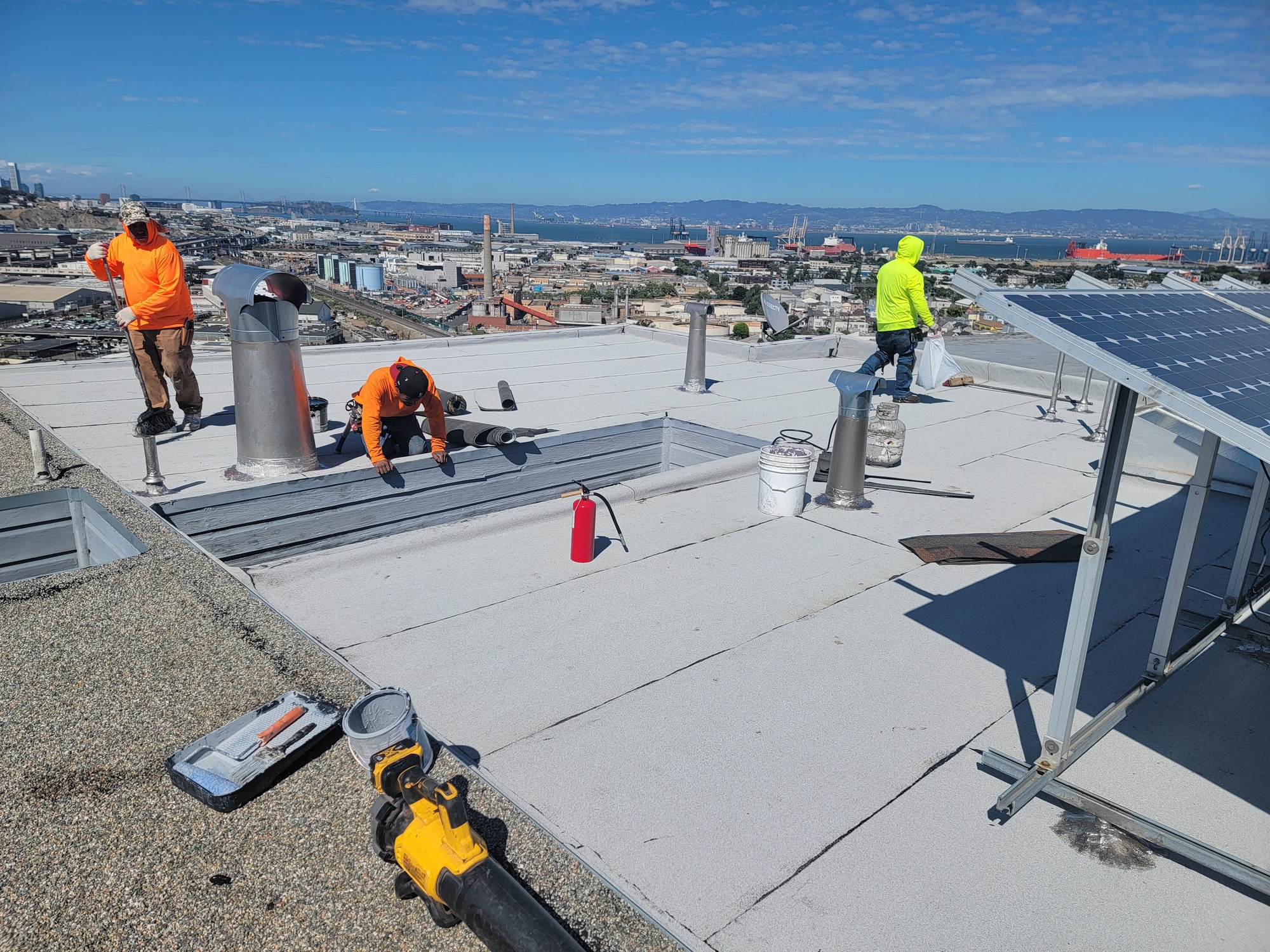 Ace Roofing crew applying protective coating to a flat roof with sweeping San Francisco Bay views