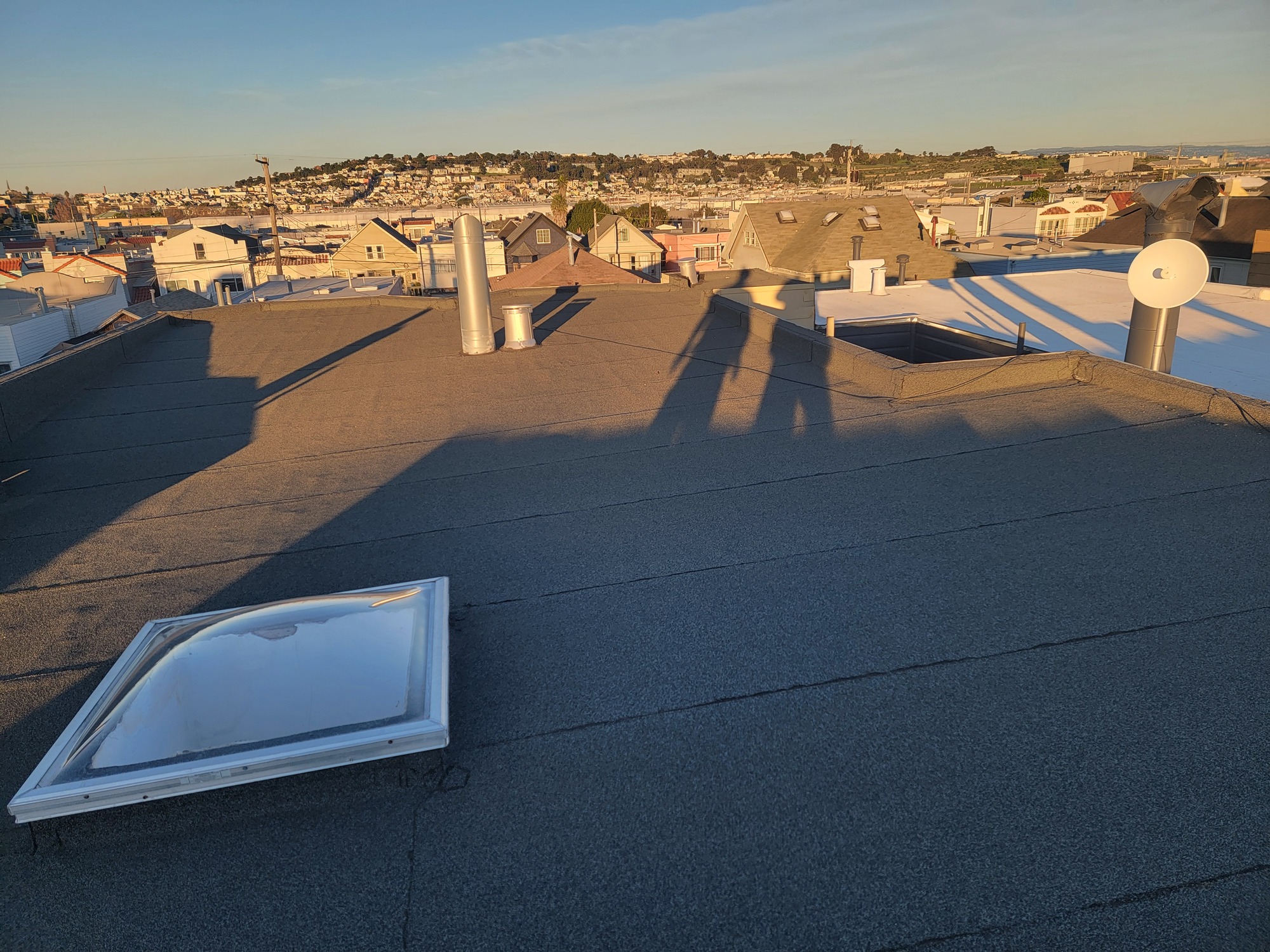 Finished cap-sheet flat roof with bubble skylight at sunset in a San Francisco neighborhood