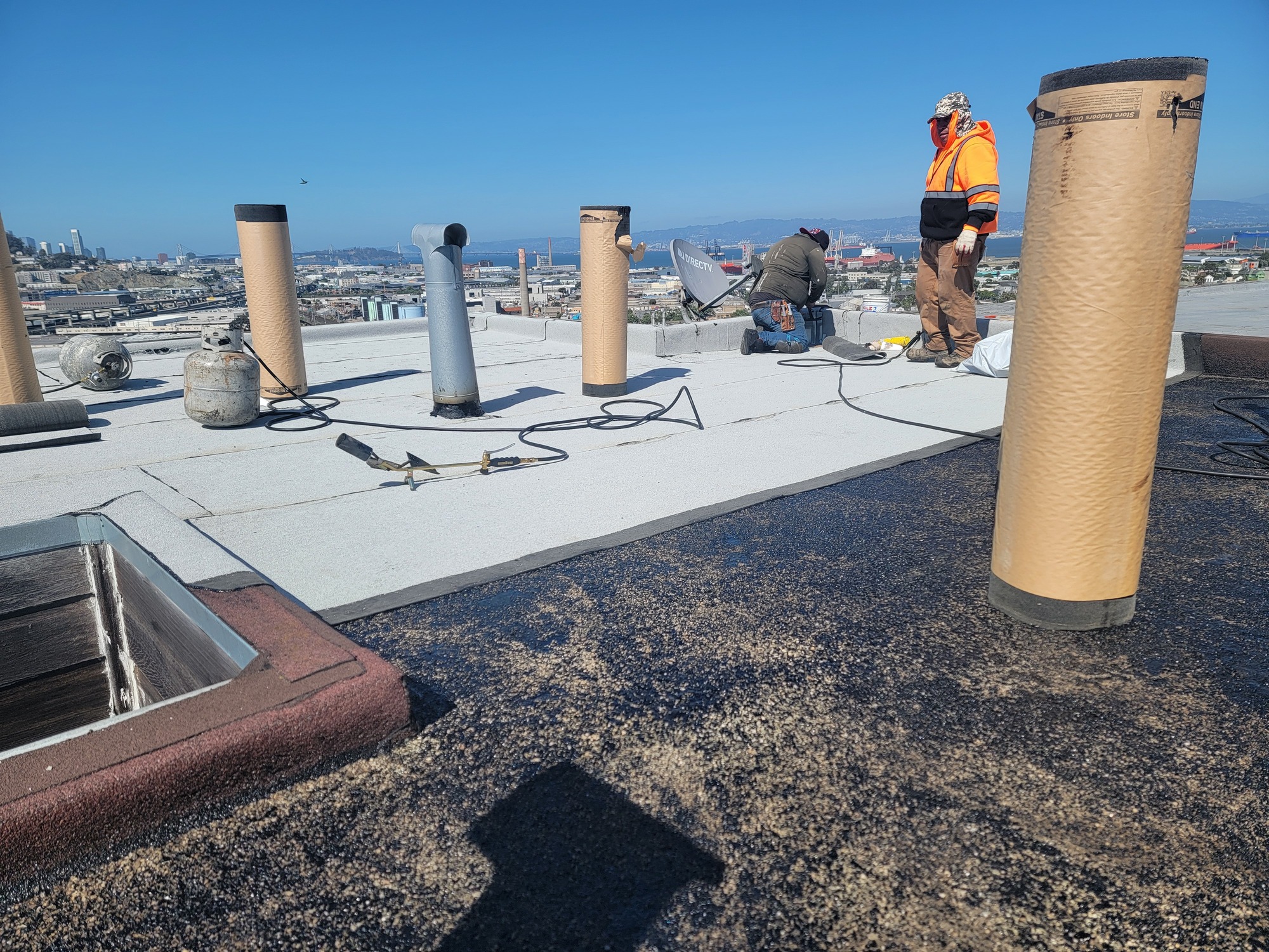 Newly installed cap-sheet flat roof with vent stacks on a San Francisco rooftop overlooking the Bay