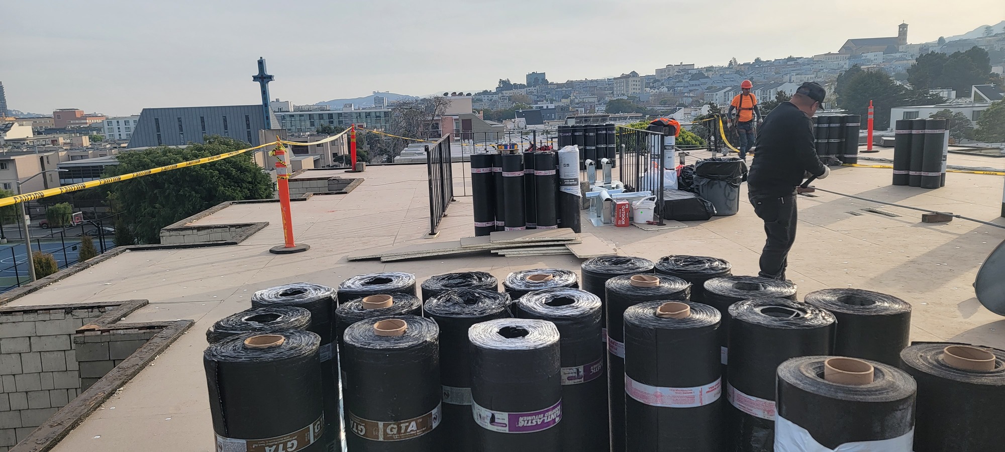 Modified bitumen rolls stacked on a San Francisco rooftop with the city skyline behind