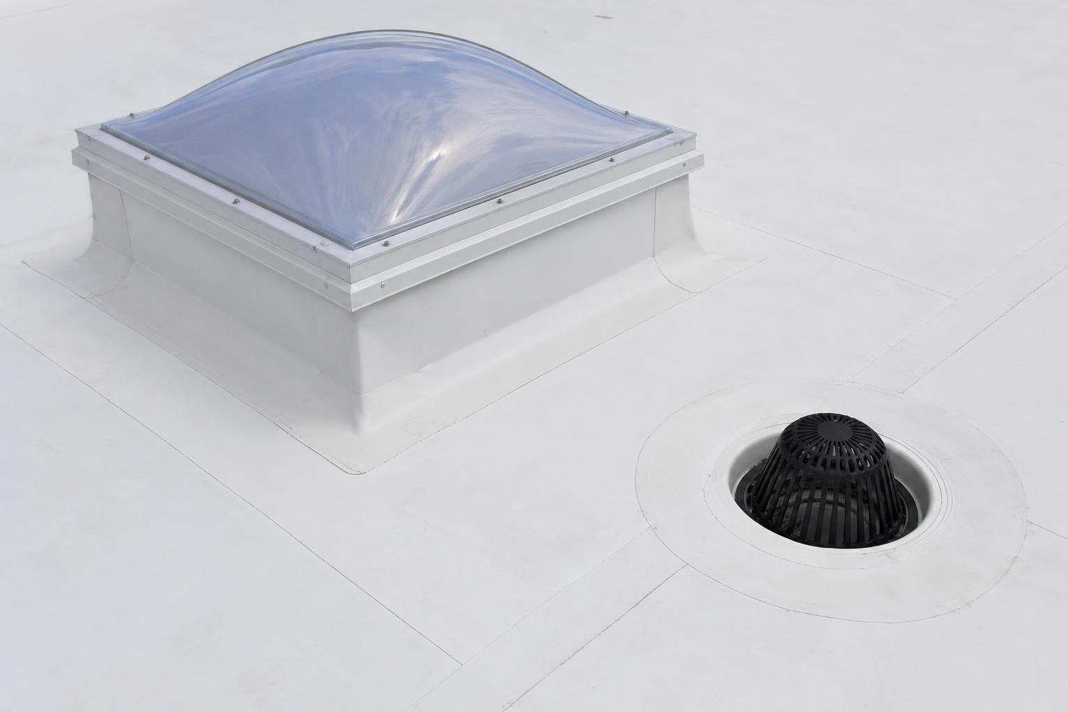 Newly installed skylight curb and roof drain with strainer dome on a white TPO flat roof